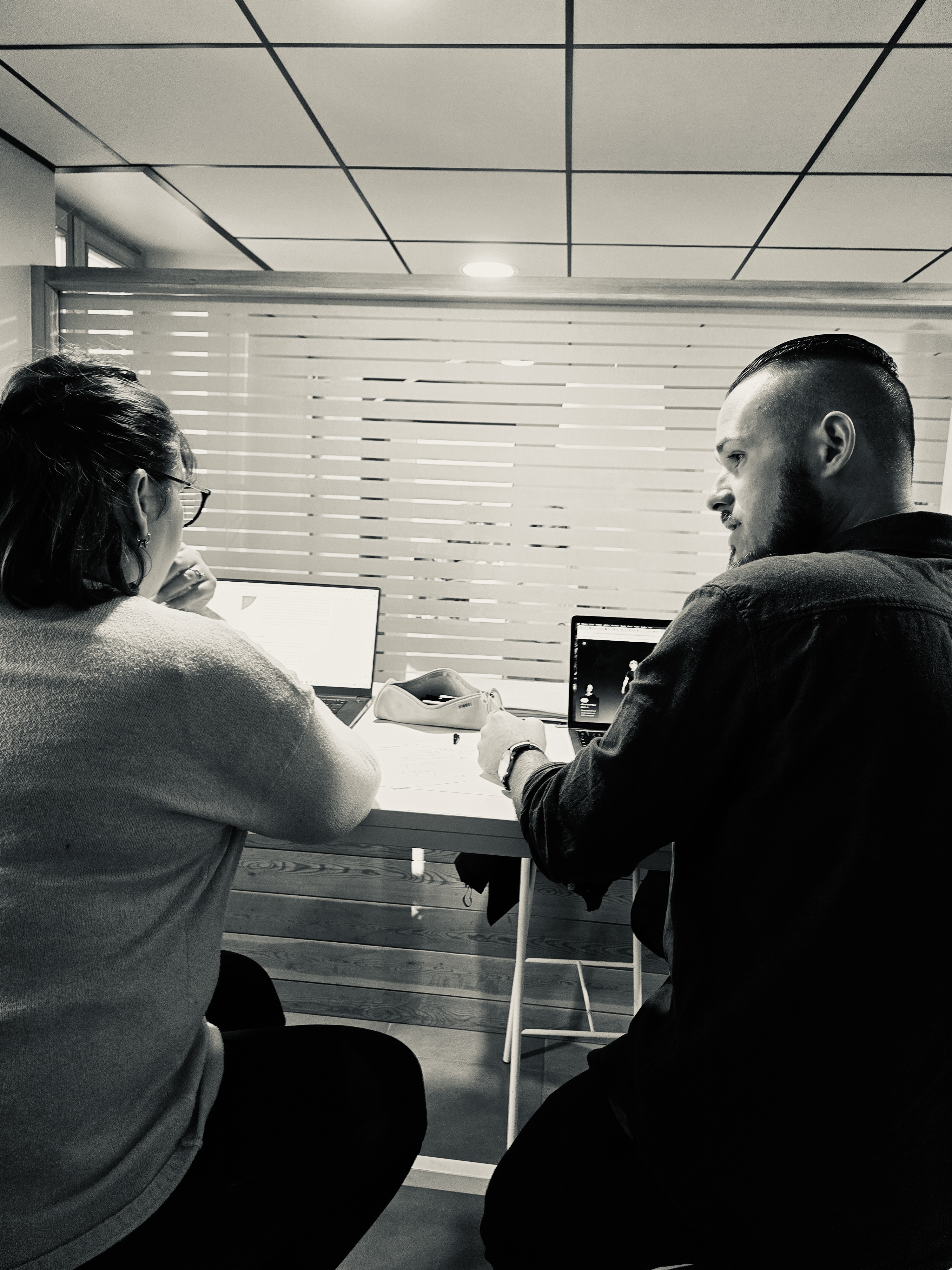 Atelier d'écoute en noir et blanc : deux personnes côte à côte devant leurs ordinateurs portables, regard tourné vers l'écran, posture de co-conception