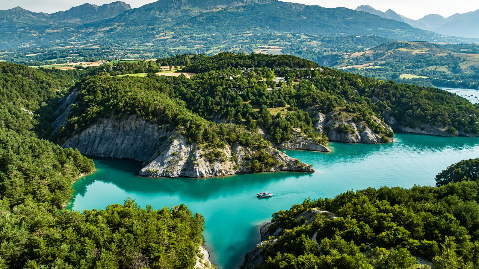 Crique aux eaux turquoise du lac de Serre-Ponçon dans les Hautes-Alpes, falaises calcaires et forêts de pins, un bateau au mouillage