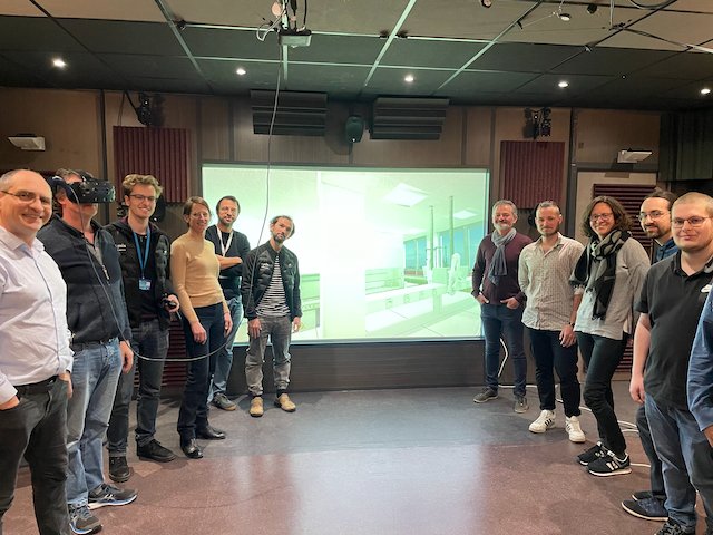 Le consortium du projet ANR RENFORCE réuni devant l'écran de projection du laboratoire virtuel, un participant équipé d'un casque de réalité virtuelle